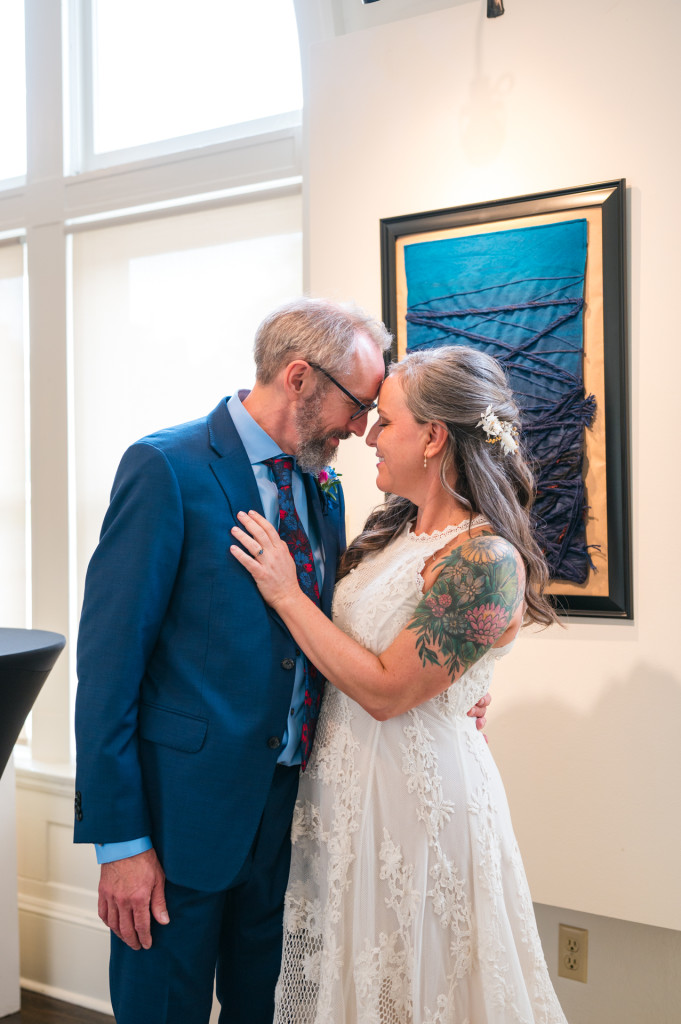 Bride and Groom standing forehead-to-forehead in art gallery