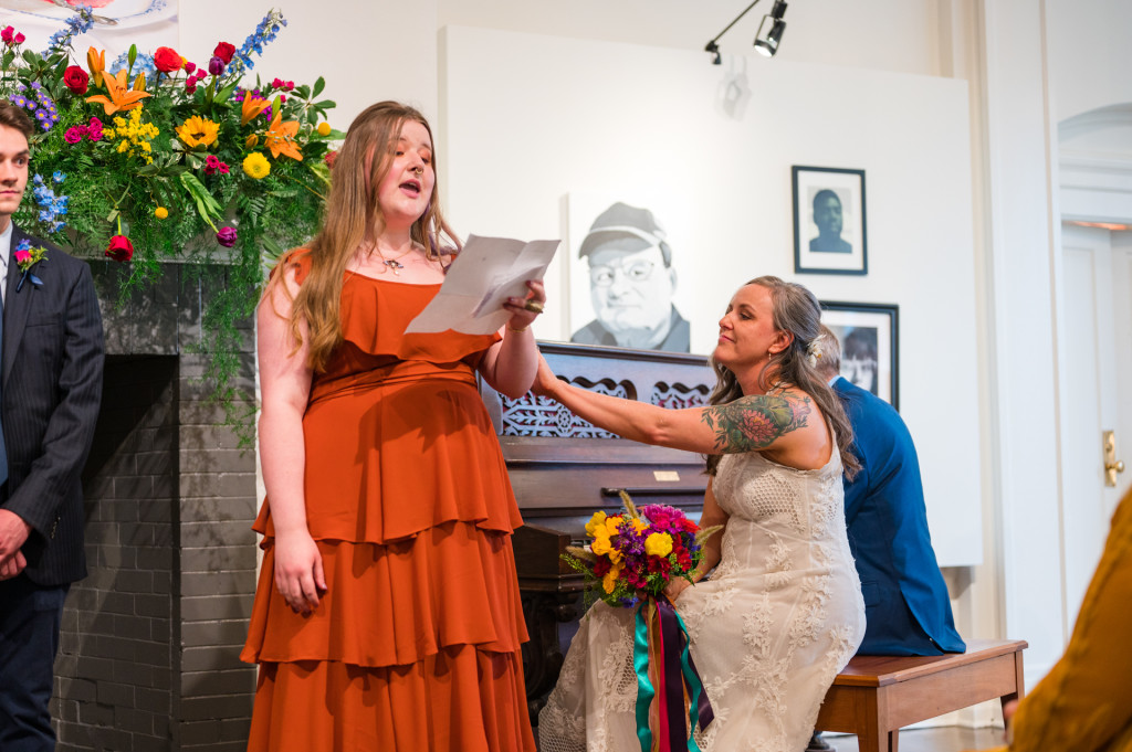 Bridesmaid in orange dress reading poem